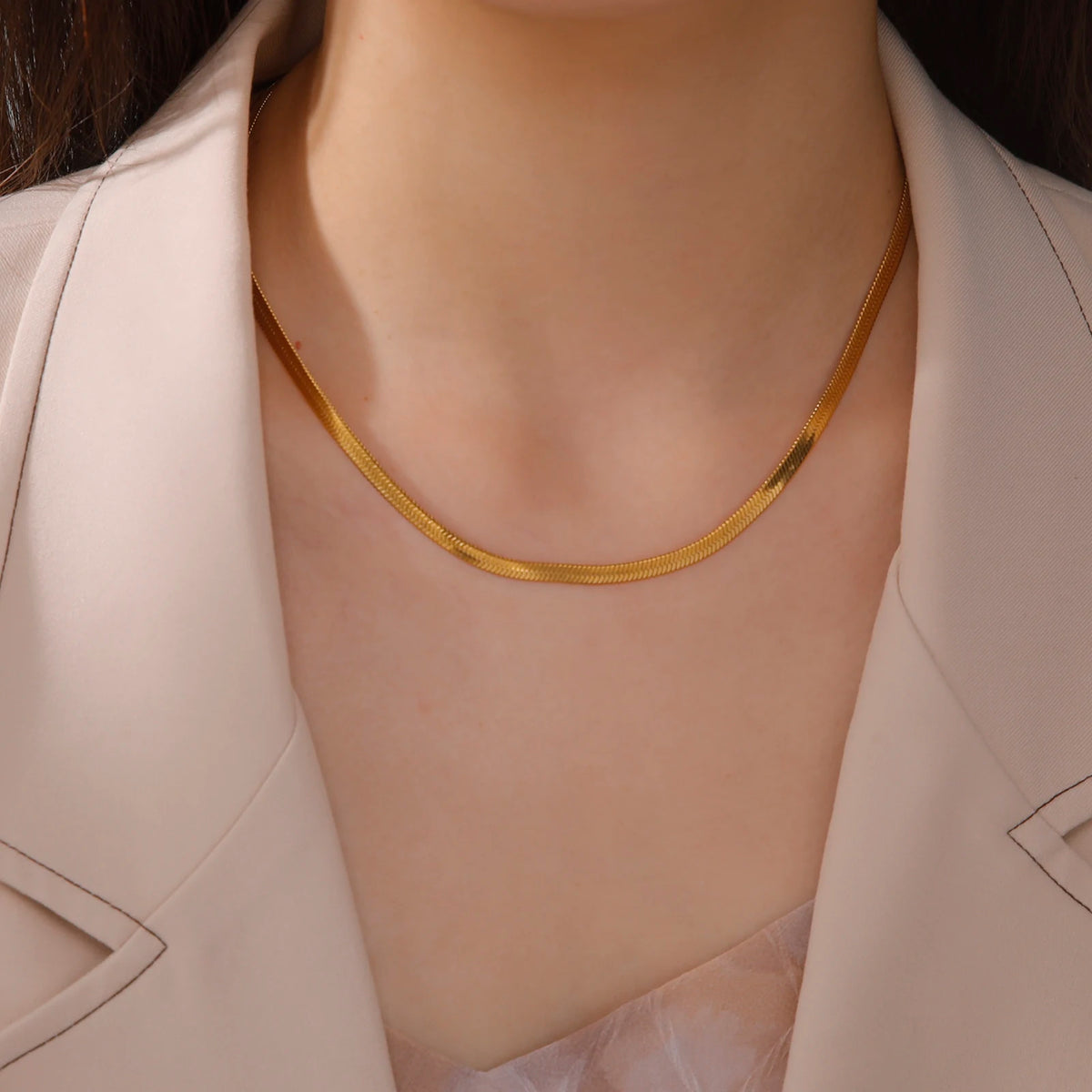 Nahaufnahme einer Frau mit goldener Edelstahl-Schlangenkette gegen ein hellbeiges Sakko.
