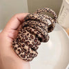 A hand is holding a coil of leopard print elastic hair ties for ponytails.