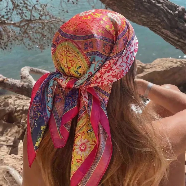 Une femme portant un foulard hijab en satin soie rose vif et orange avec des motifs floraux, à l'extérieur.