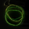 A coil of luminous glow-in-the-dark green beads, resembling anklets, rests on a dark surface.