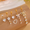 A set of five gold stainless steel dangled belly button rings with various charms and designs displayed on a beige surface.