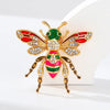 Broche ton or avec motif abeille baroque en émail rouge, vert et or, et strass clairs.