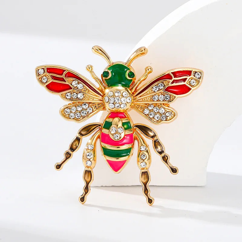 Broche ton or avec motif abeille baroque en émail rouge, vert et or, et strass clairs.