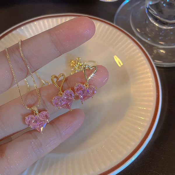Eine Hand hält eine rosa Kristallherz-Kette mit goldener Kette und herzförmigen Anhängern auf einer weißen Platte.