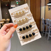 A hand holds a display of gold-toned pearl and black bead brooch pins arranged on a white card.
