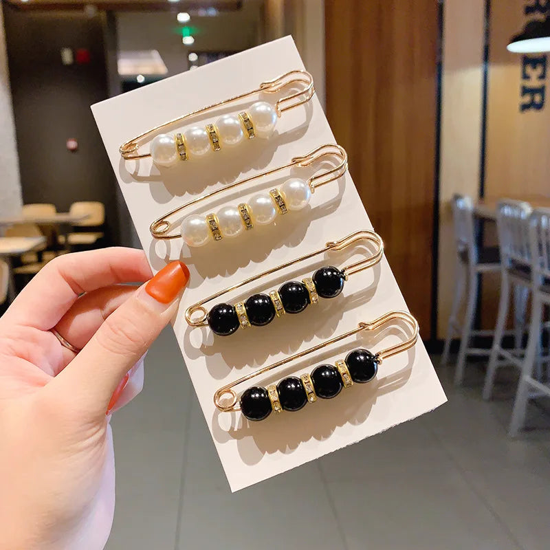 A hand holds a display of gold-toned pearl and black bead brooch pins arranged on a white card.