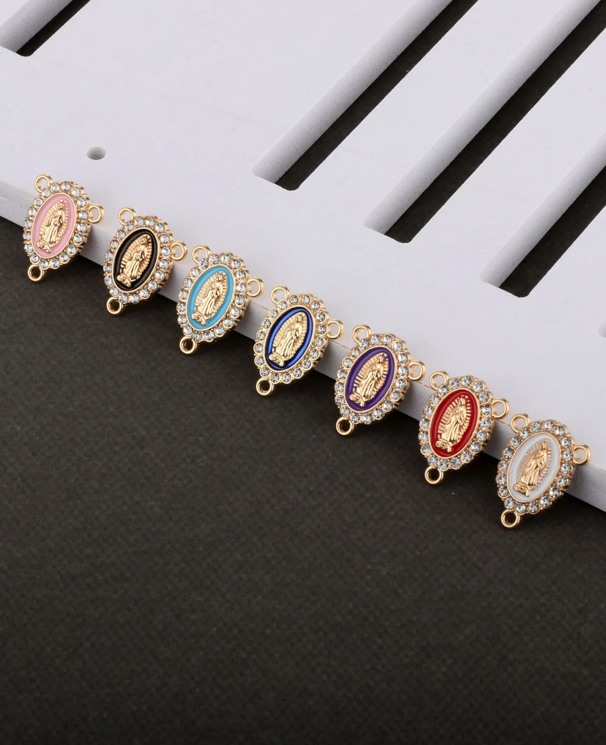 A line of gold-toned rosary connectors featuring oval beads in pink, blue, purple, and red with gold accents.