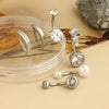A collection of surgical stainless steel belly button rings and piercings displayed on a clear plastic dish.