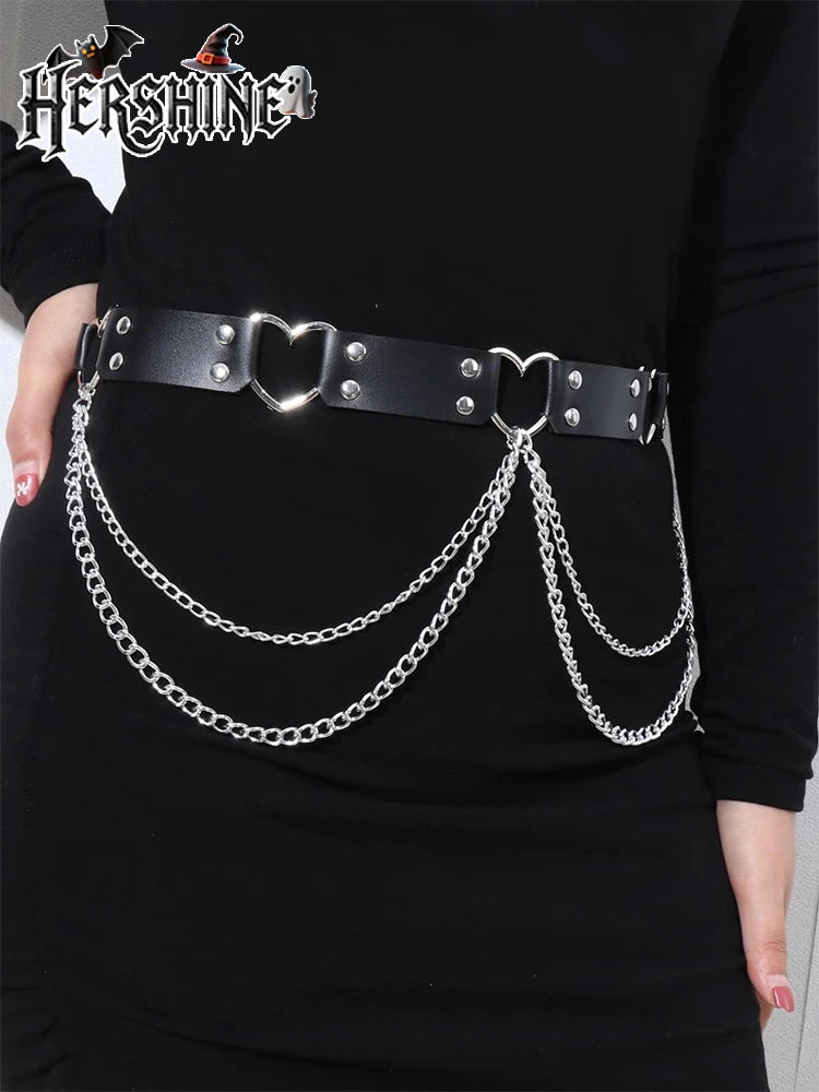 Un vestido negro con cinturón de cadena de corazón plateada y correas de cuero y herrajes plateados.