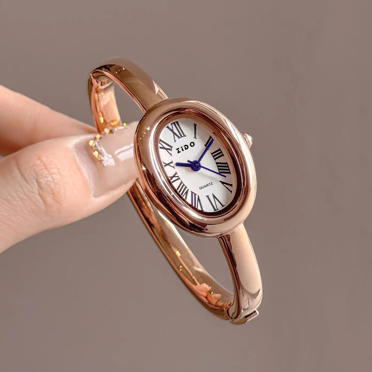 A close-up shot of a rose gold vintage quartz analog watch with an oval face being held by a hand.