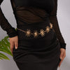 A woman wearing a black dress with a gold heart waist chain body jewelry detail.