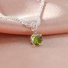 A delicate silver-plated chain necklace featuring a green gemstone pendant resting on pink fabric.