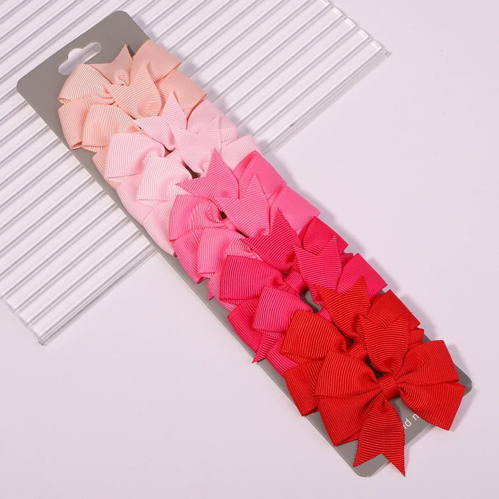 A collection of pink, magenta, and red handmade ribbon bow hair clips arranged on a striped background.