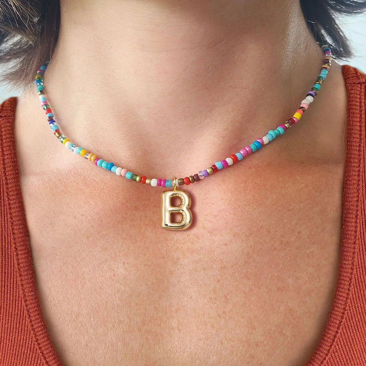 Primer plano de un collar de cuentas con un dije de la letra B, usado alrededor del cuello de una mujer.