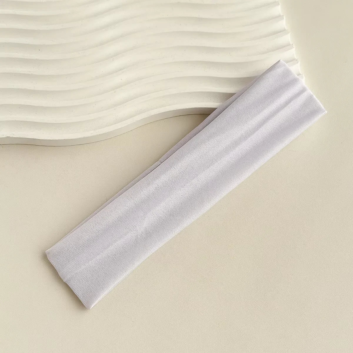 A white fabric headband is shown lying next to a wavy background.