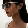 A woman wearing round metal beads sunglasses with a chain necklace and white top.