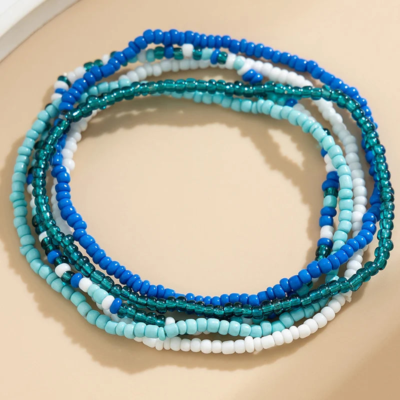 A stack of multi-layered anklets featuring beads in shades of blue, teal, and white.