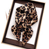 A luxury leopard print silk scarf tied in a bow displayed in a brown box.
