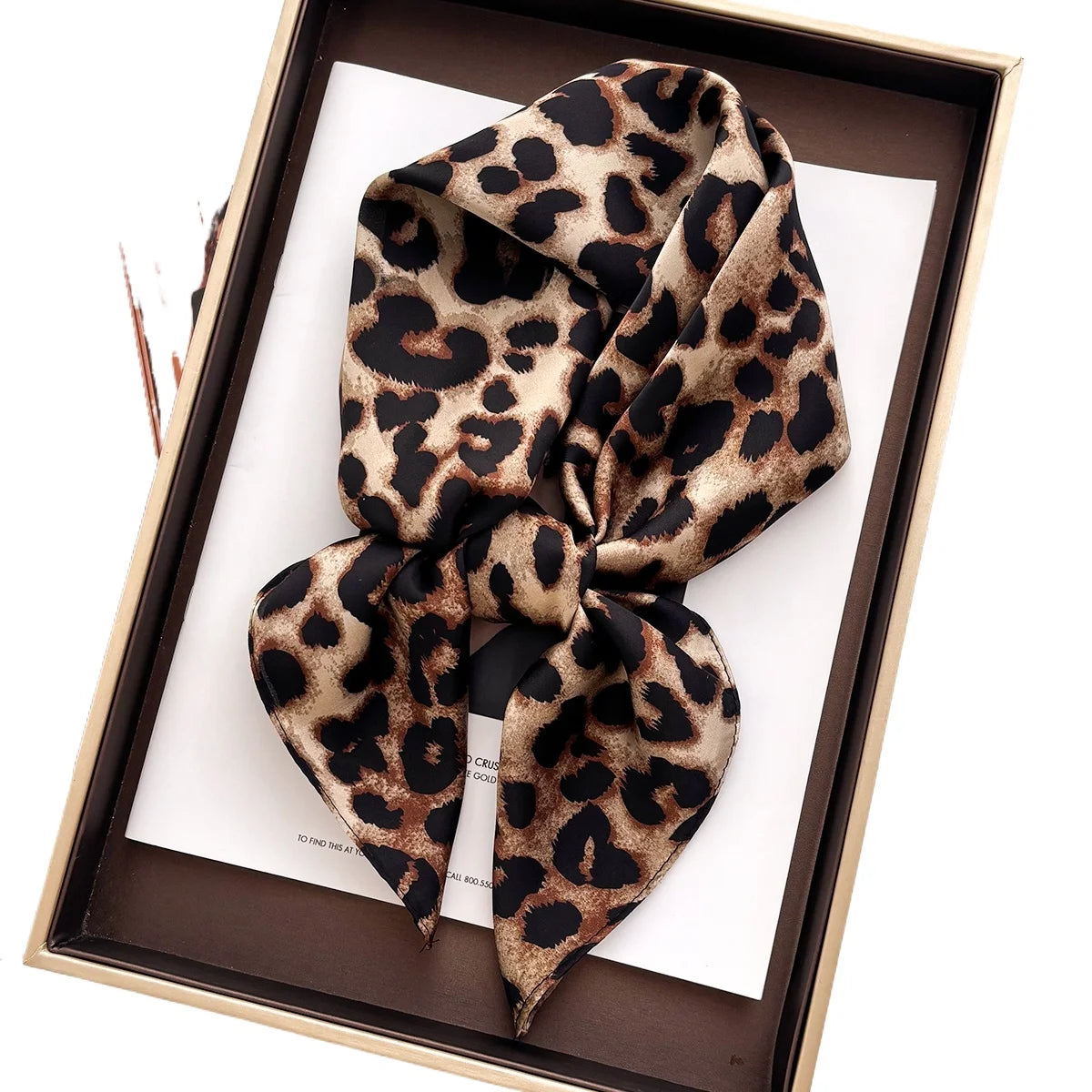 A luxury leopard print silk scarf tied in a bow displayed in a brown box.