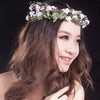 A woman with long brown hair wears a bohemian flower headband featuring pink and white flowers.