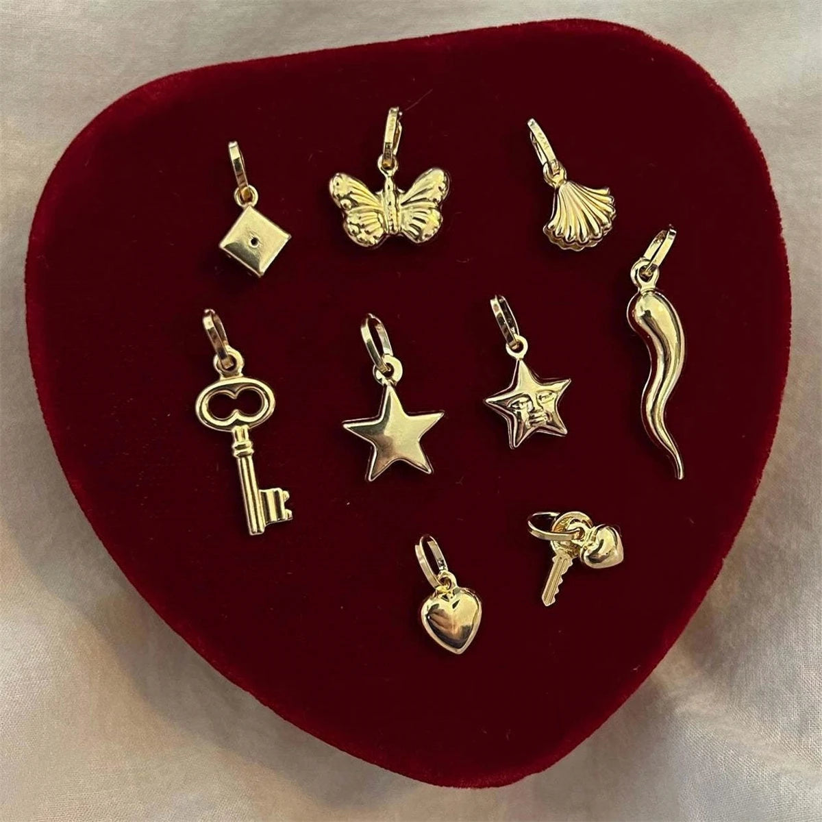 Gold plated butterfly key pendant charm displayed on a dark red velvet surface.