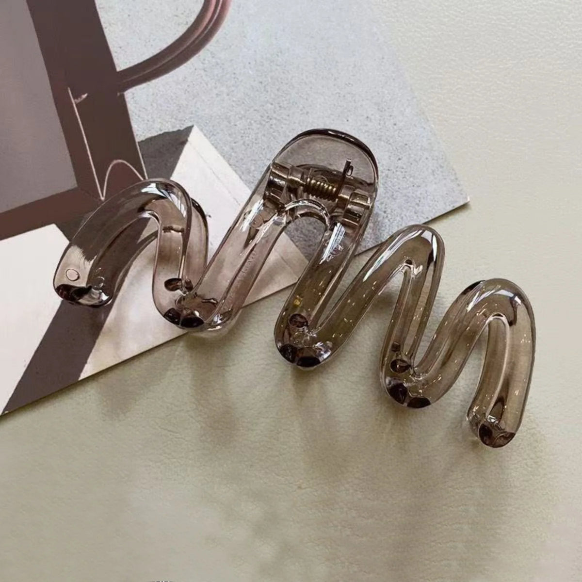 A pair of high-gloss amber hair clips are shown coiled on a light surface.