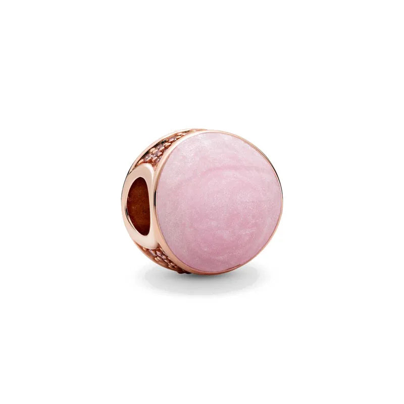 A round rose gold charm pendant with a pink, translucent stone and textured metal setting.
