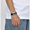 Nahaufnahme eines Mannes Handgelenks mit einem schwarzen geflochtenen Lederarmband an einem weißen T-Shirt.