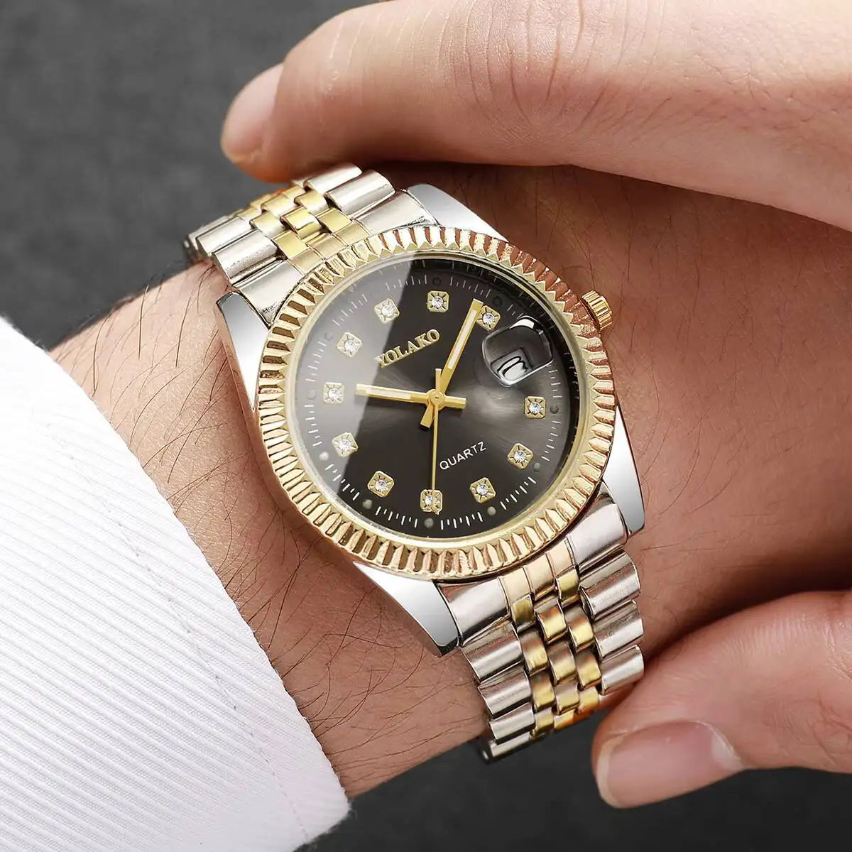A silver and gold-toned quartz wristwatch with a black dial and rhinestone accents is worn on a wrist.