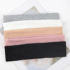 A stack of black, pink, beige, white, and gray knitted elastic headbands for hair and face.