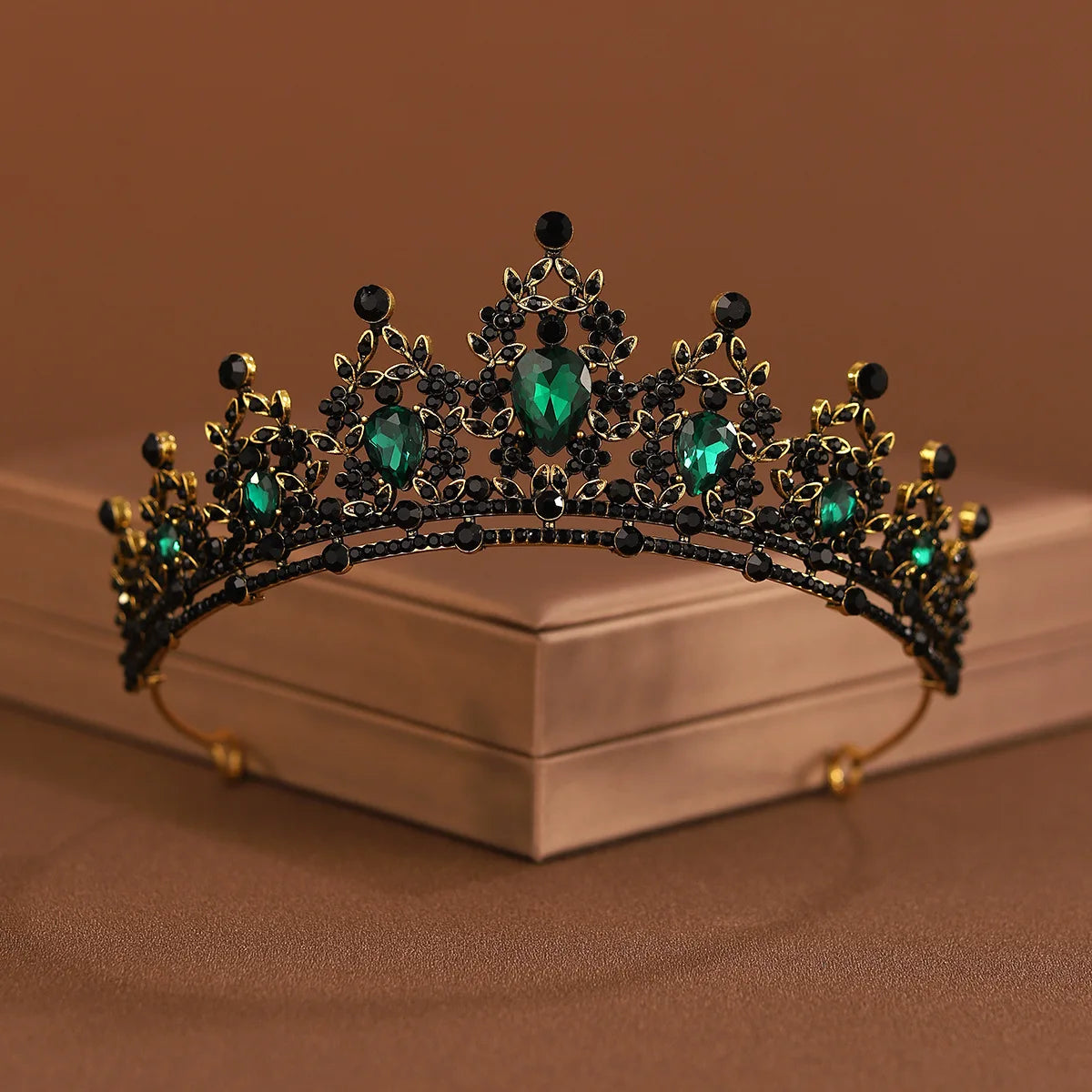 A dark gold and black crystal baroque bridal tiara headpiece with green gemstones on a white box.