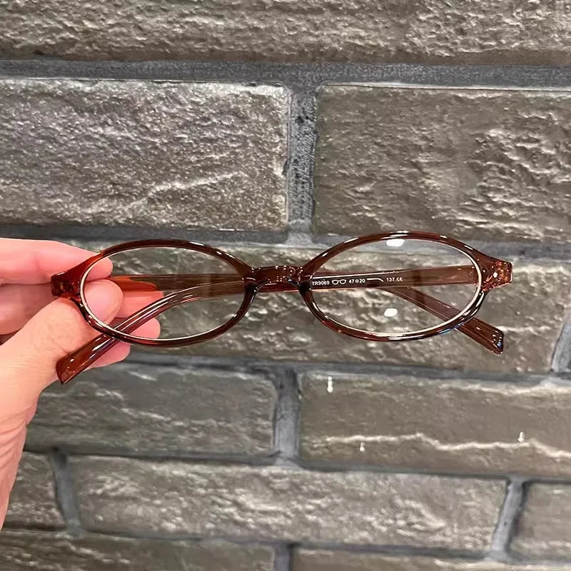Une paire de lunettes ovales teintées de brun est tenue contre un mur de briques grises.