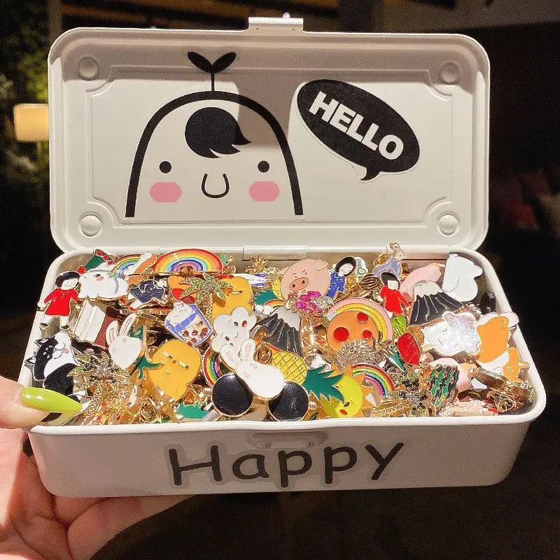 A white tin box with a lid and an open compartment filled with colorful metal pin badges and a sign that reads Happy