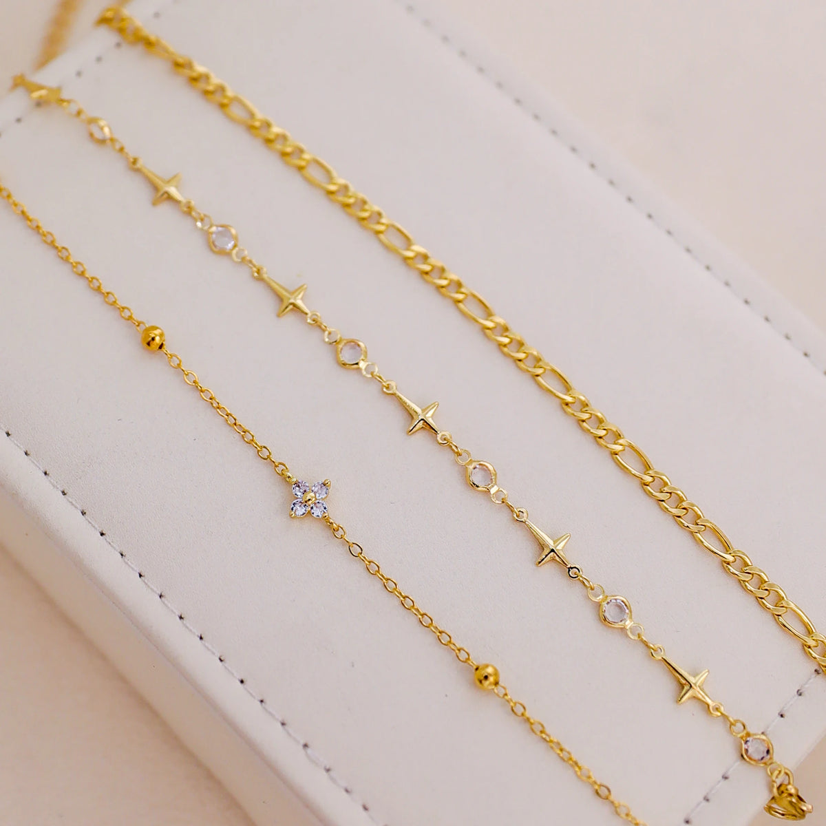 A set of gold-colored handmade crystal cross anklets displayed on a white surface.
