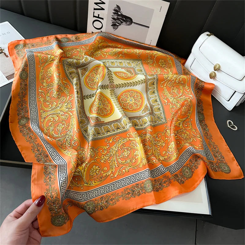 An orange silk scarf with gold and cream patterns is displayed on a dark surface.