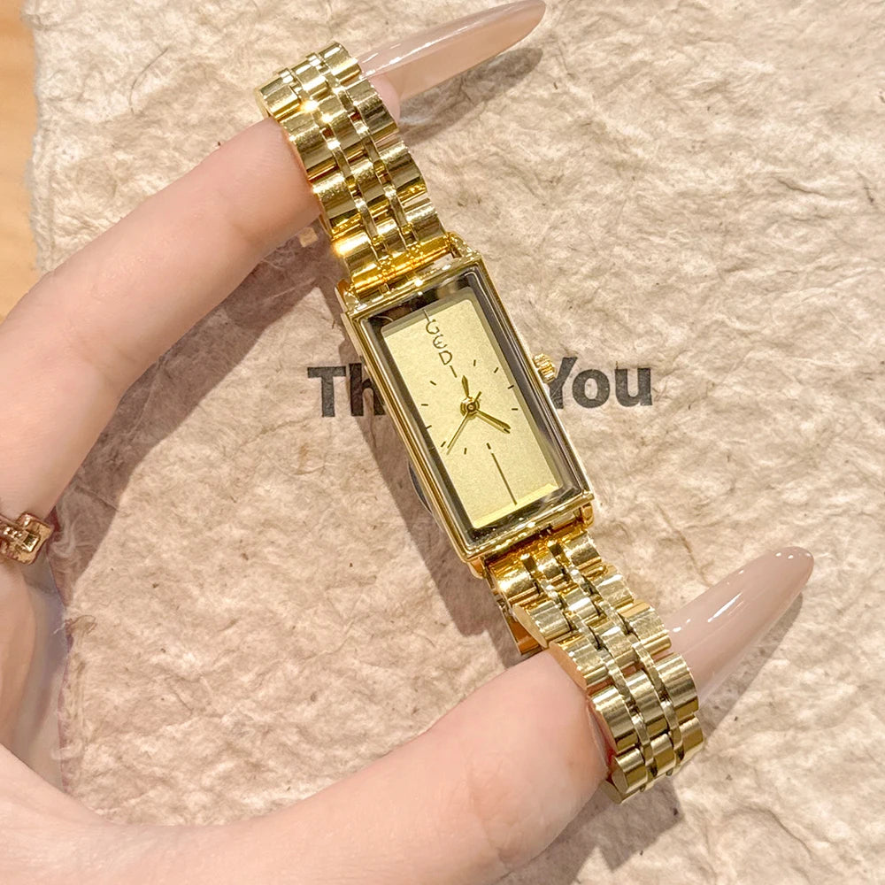 A close-up shot of a vintage gold stainless steel quartz watch worn on a finger against a beige background.