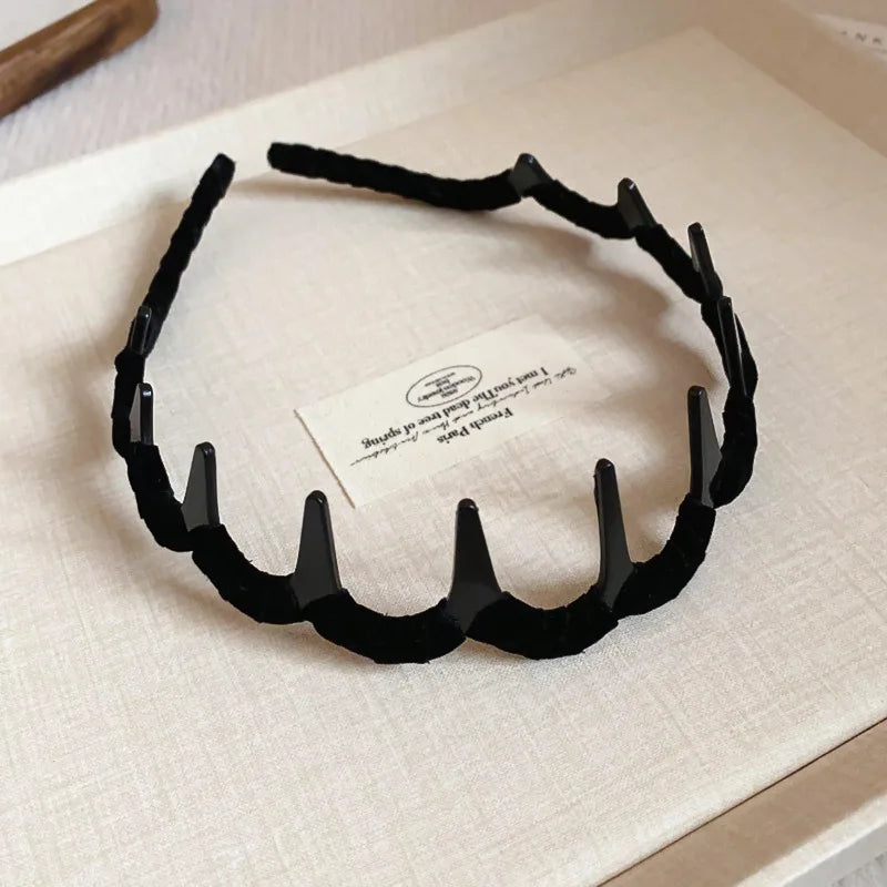 Black resin wave toothed headband for women displayed on a light surface.