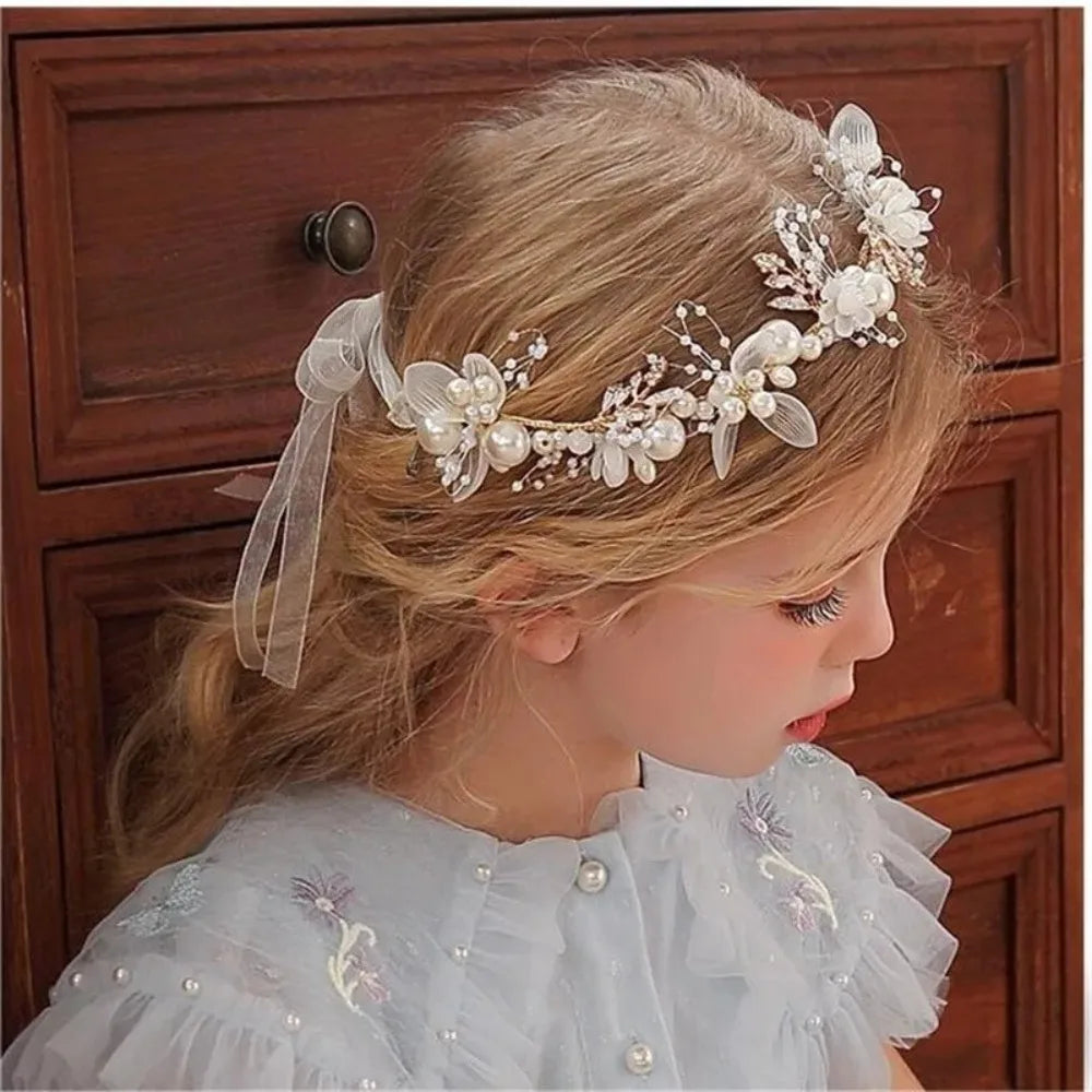 A young girl wearing an elegant floral wreath headband and a sheer white dress.