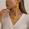 A close-up of a woman wearing a gold floral pendant necklace and matching earrings against a light sweater.