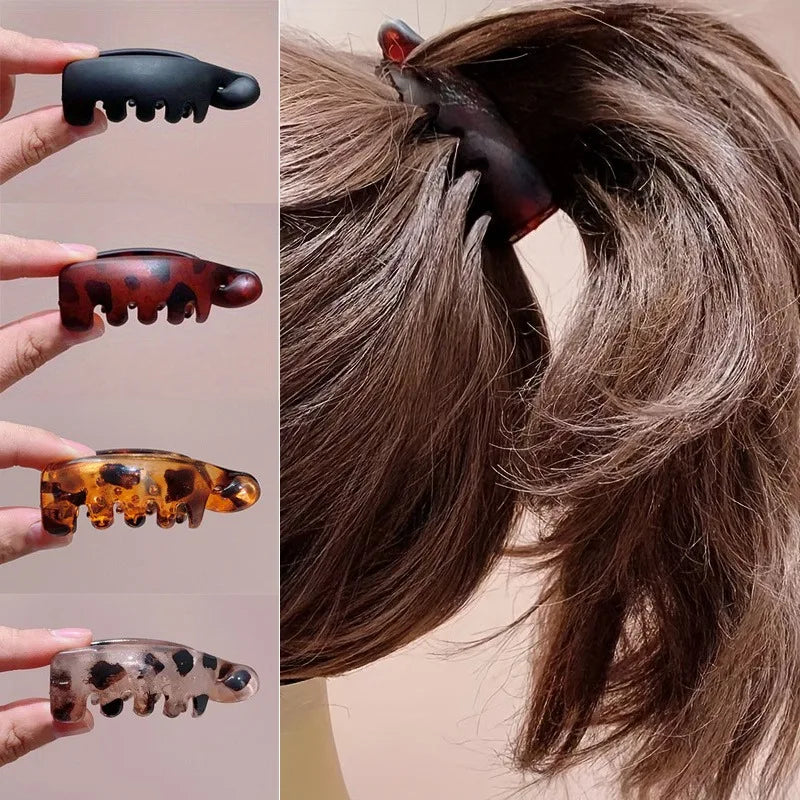 Un juego de cuatro clips para el pelo con forma de plátano en varios colores translúcidos y opacos, contra un fondo de cabell