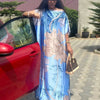 Eine Frau in einem blau-rosa Boho-Seidenbedruckten Kaftan steht neben einem roten Auto.