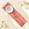 A pink plaid fabric headband with a white button and daisies, displayed on a light background.