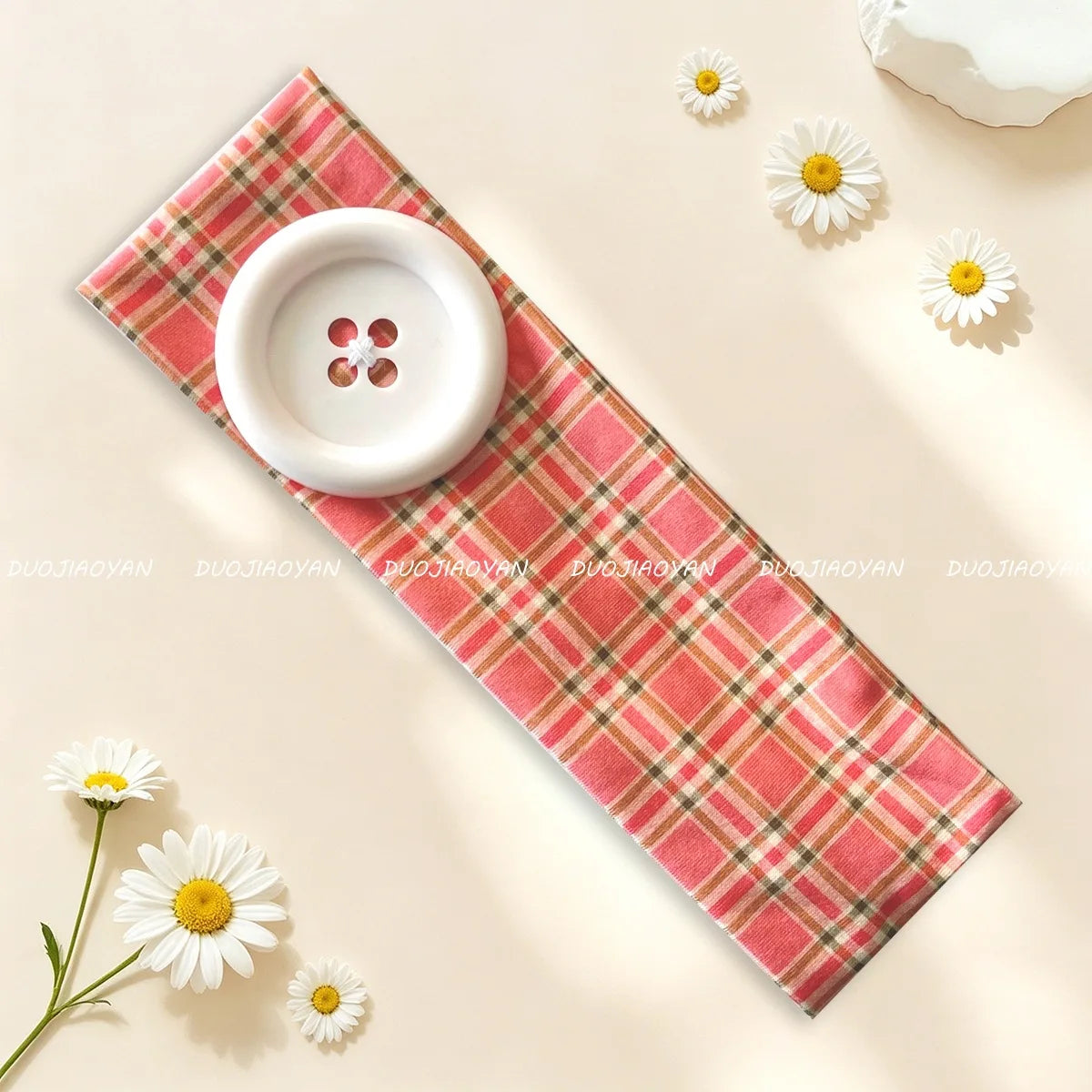 A pink plaid fabric headband with a white button and daisies, displayed on a light background.