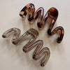 A pair of high-gloss amber hair clips shaped like spirals, displayed against a white background.