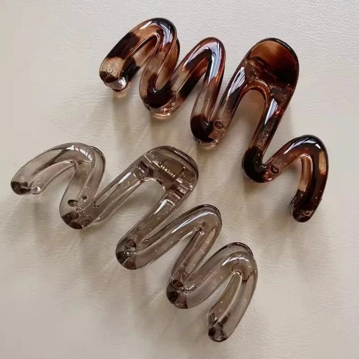 A pair of high-gloss amber hair clips shaped like spirals, displayed against a white background.