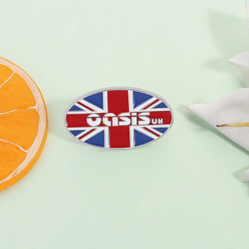 Broche émail avec le drapeau du Royaume-Uni et le mot Oasis en blanc sur fond argenté.