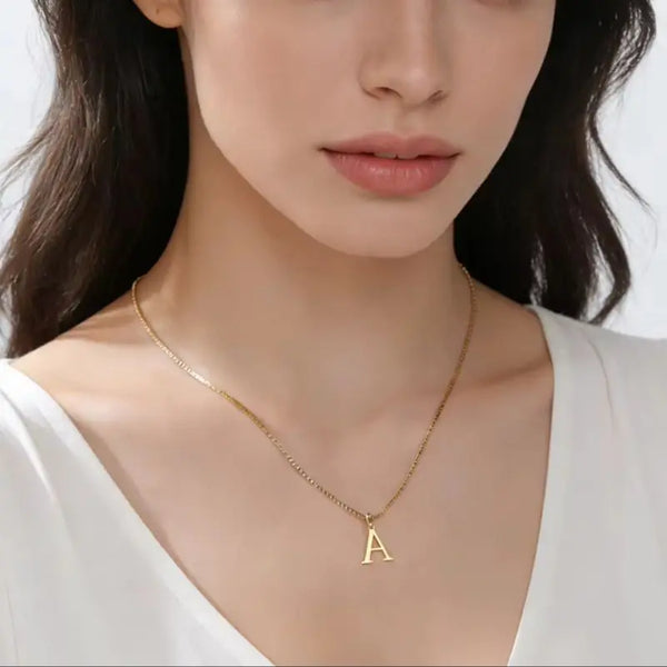 A gold initial letter necklace worn by a woman against a light background.