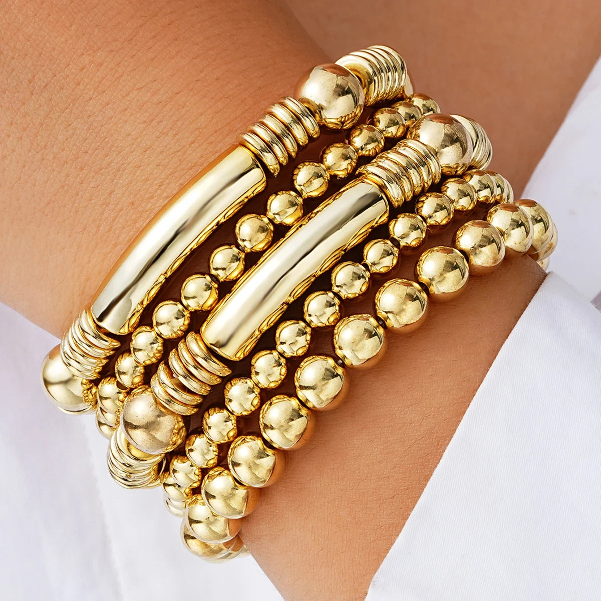A stack of gold-colored beaded bracelets worn on a wrist.