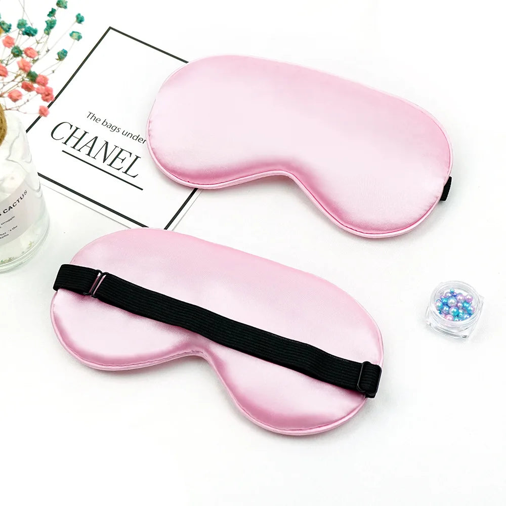 Pink silk sleep mask with a black strap shown next to a luxury bag brand label