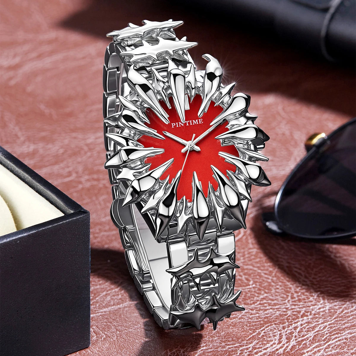 Silver watch with dragon scale design and red dial resting on a brown leather surface.